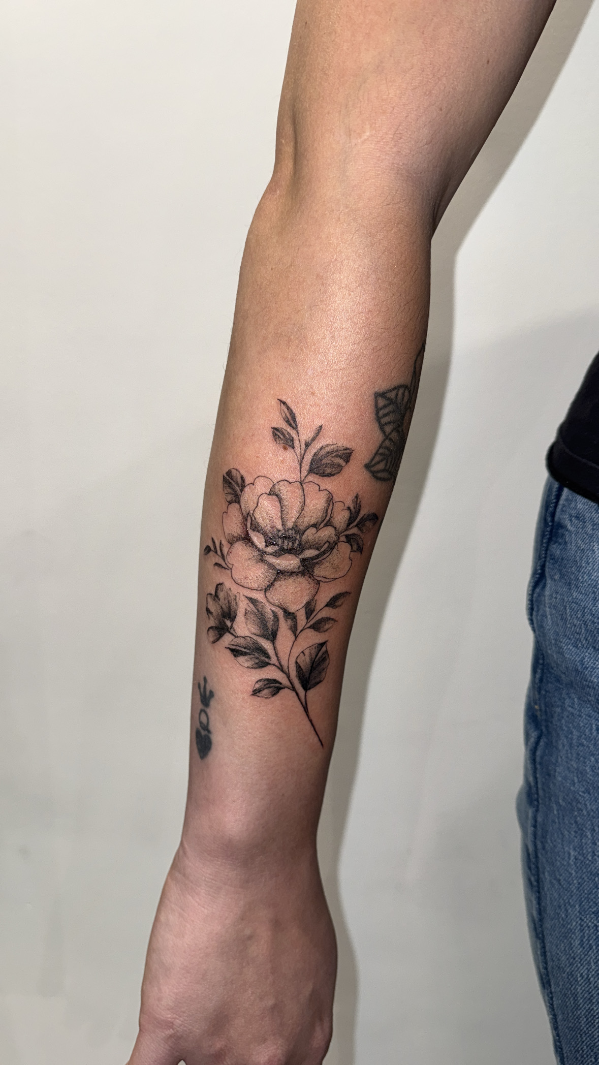 Black and grey floral peony tattoo with fine linework on the forearm